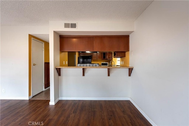 kitchen with dark hardwood / wood-style flooring, a kitchen breakfast bar, kitchen peninsula, and a textured ceiling