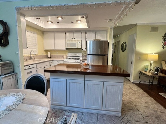 kitchen with stainless steel refrigerator, white cabinetry, sink, range, and a raised ceiling