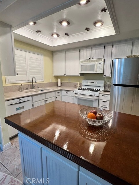 kitchen featuring sink, ornamental molding, light tile patterned floors, a raised ceiling, and white appliances