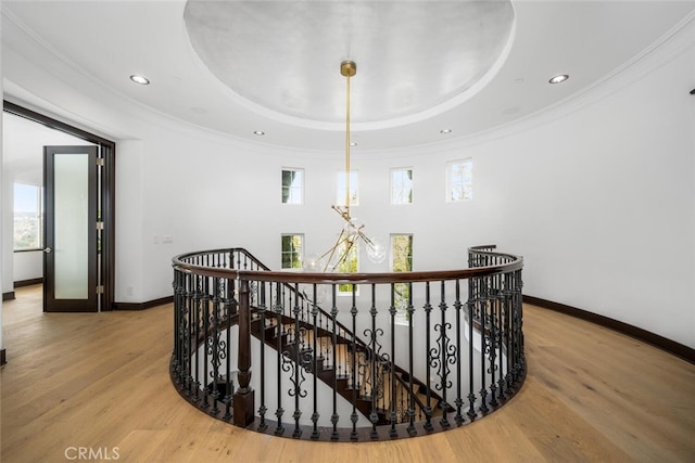 hall with a healthy amount of sunlight, ornamental molding, a tray ceiling, and light hardwood / wood-style floors