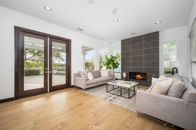 living room featuring a tiled fireplace, hardwood / wood-style floors, and french doors