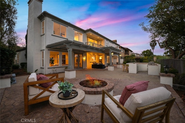 back house at dusk with a patio, an outdoor kitchen, an outdoor living space with a fire pit, and a pergola