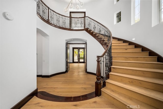 staircase with hardwood / wood-style flooring, a towering ceiling, and an inviting chandelier