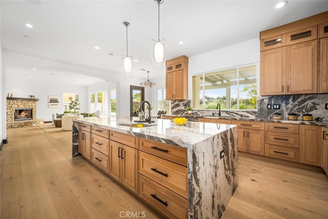 kitchen featuring a large island with sink, light wood-type flooring, light stone counters, and decorative light fixtures