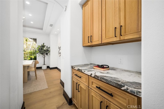 kitchen featuring a raised ceiling, light hardwood / wood-style flooring, and dark stone counters