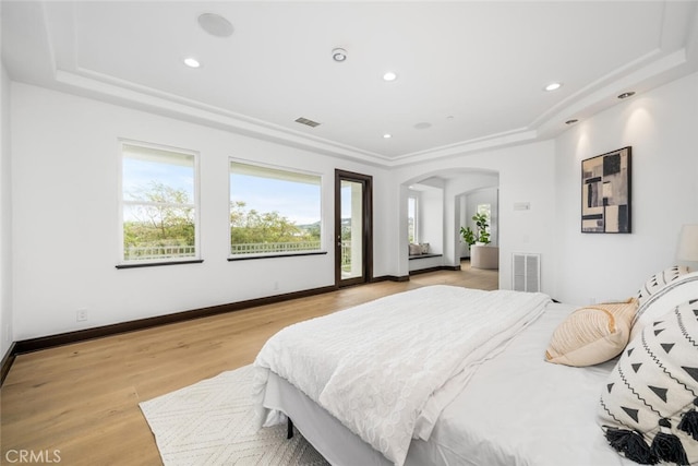 bedroom with a raised ceiling, access to outside, and light hardwood / wood-style flooring