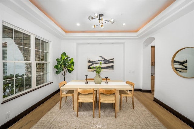 dining space featuring a raised ceiling, light hardwood / wood-style flooring, and a notable chandelier