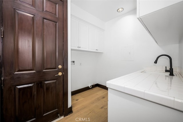 laundry room featuring cabinets, sink, and light hardwood / wood-style flooring