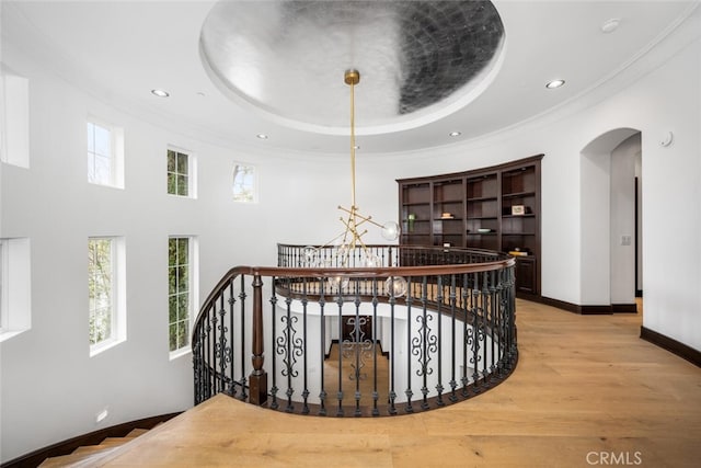 staircase featuring crown molding, hardwood / wood-style floors, a chandelier, and a tray ceiling