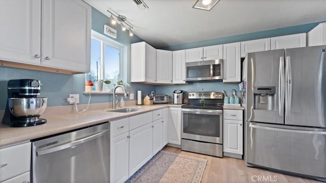 kitchen with rail lighting, sink, white cabinets, stainless steel appliances, and light hardwood / wood-style flooring