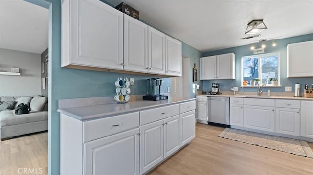 kitchen with white cabinetry, sink, stainless steel dishwasher, and light hardwood / wood-style flooring