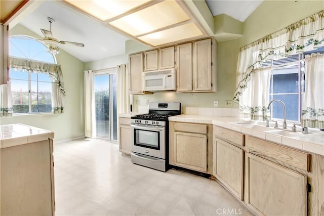 kitchen with sink, ceiling fan, vaulted ceiling, stainless steel gas range oven, and tile countertops