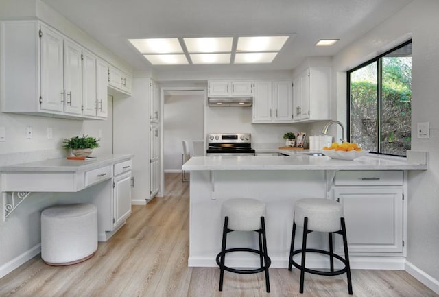 kitchen with a kitchen breakfast bar, kitchen peninsula, white cabinets, and stainless steel electric range oven