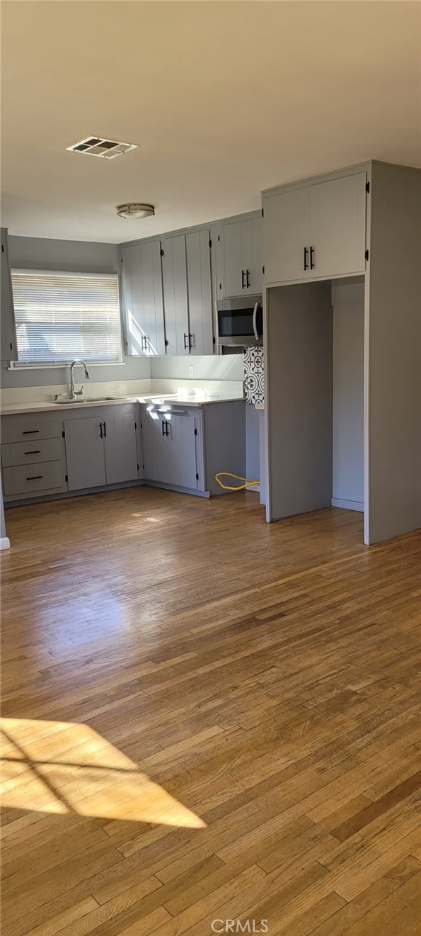 kitchen featuring stainless steel microwave, wood finished floors, a sink, and gray cabinetry