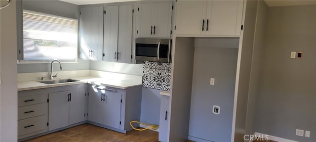 kitchen with light wood-style flooring, stainless steel microwave, light countertops, and a sink