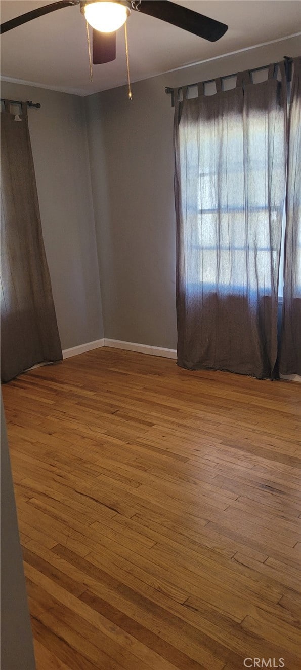 empty room featuring hardwood / wood-style flooring, baseboards, and a ceiling fan