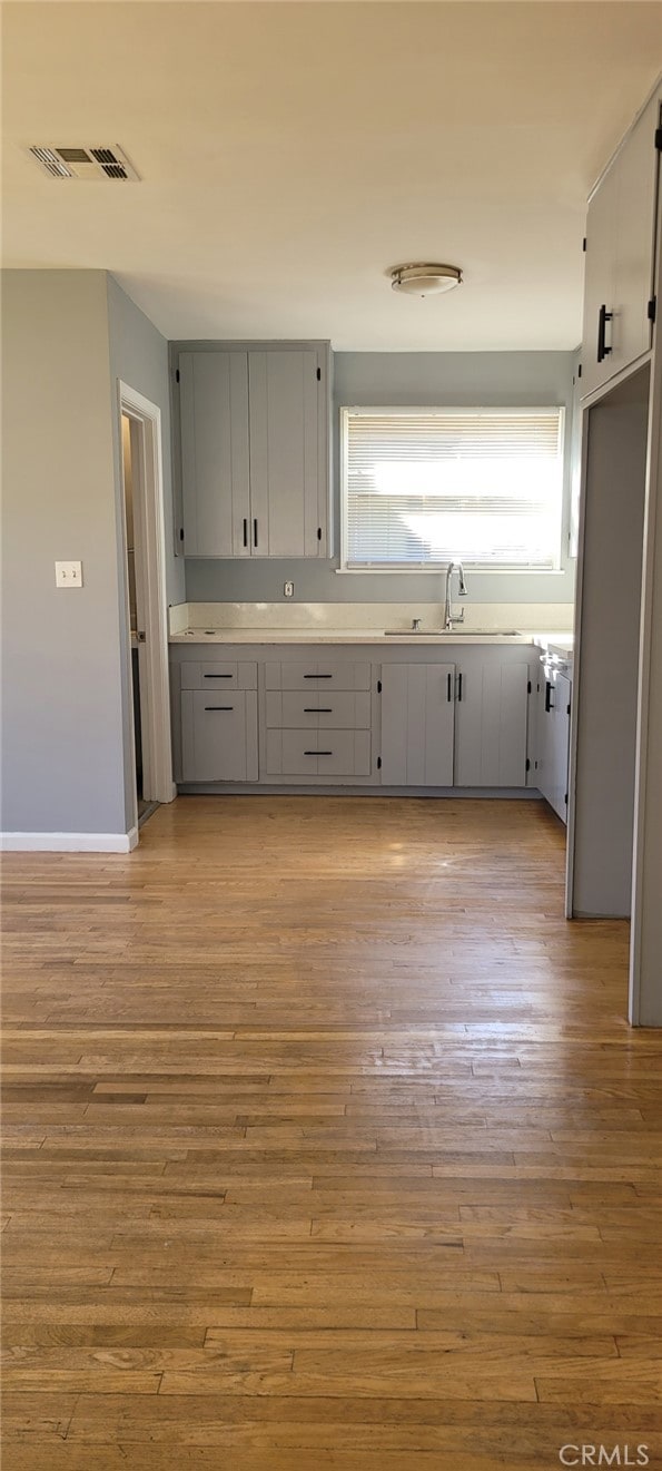 kitchen featuring visible vents, light countertops, gray cabinetry, light wood-type flooring, and a sink