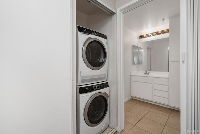 clothes washing area with sink, light tile patterned flooring, and stacked washing maching and dryer