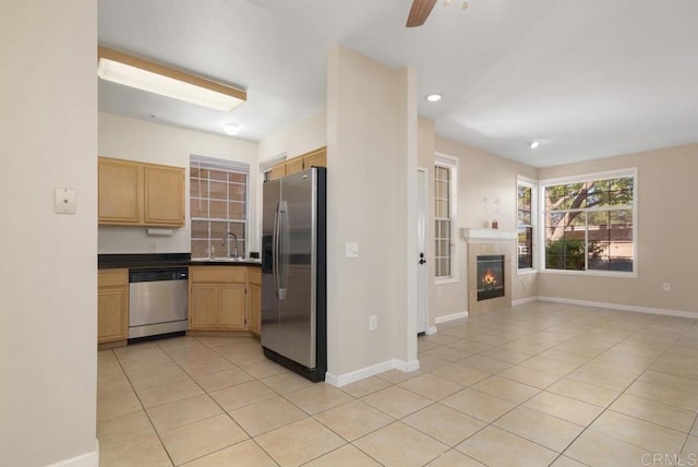 kitchen with light brown cabinets, appliances with stainless steel finishes, a tile fireplace, and light tile patterned floors