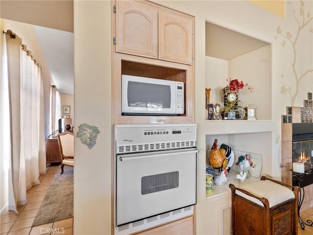 kitchen featuring white appliances, light tile patterned floors, light countertops, light brown cabinets, and a fireplace