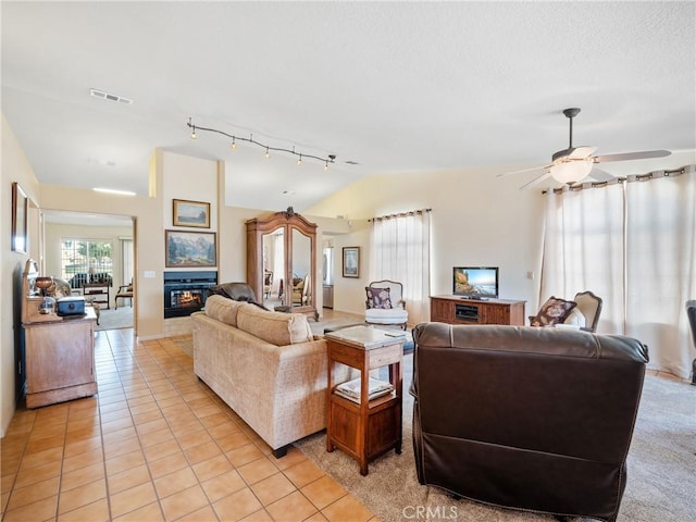 living room with light tile patterned floors, visible vents, a glass covered fireplace, lofted ceiling, and ceiling fan