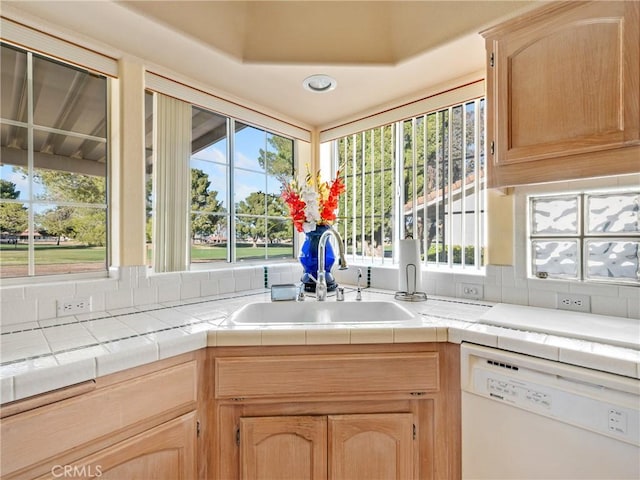 kitchen with tile counters, dishwasher, a sink, and light brown cabinetry