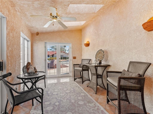 living area featuring light tile patterned floors, a textured wall, french doors, and a skylight