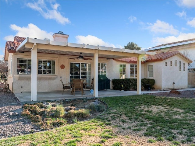 rear view of house with ceiling fan, a chimney, a patio area, and stucco siding