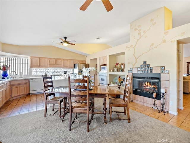 dining space featuring light tile patterned floors, ceiling fan, a tile fireplace, and lofted ceiling