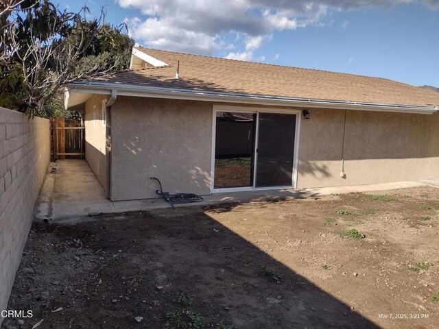 back of house with a shingled roof, fence, and stucco siding