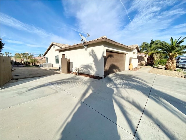 view of home's exterior with a garage, concrete driveway, fence, central AC, and stucco siding