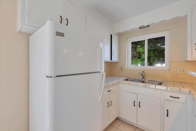 kitchen with tile counters, sink, white fridge, and white cabinets