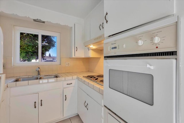 kitchen featuring tile countertops, oven, sink, and white cabinets