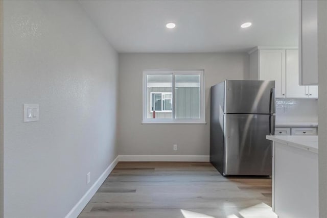 kitchen with stainless steel fridge, light hardwood / wood-style floors, and white cabinets