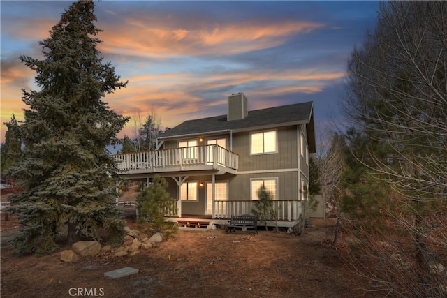 back house at dusk with a balcony and a deck