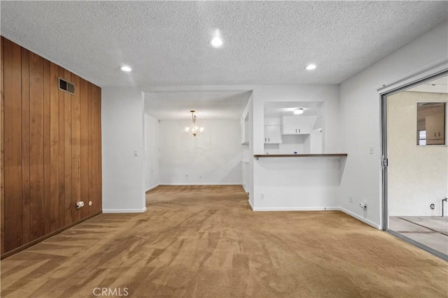 unfurnished living room featuring light carpet, a notable chandelier, a textured ceiling, and wood walls