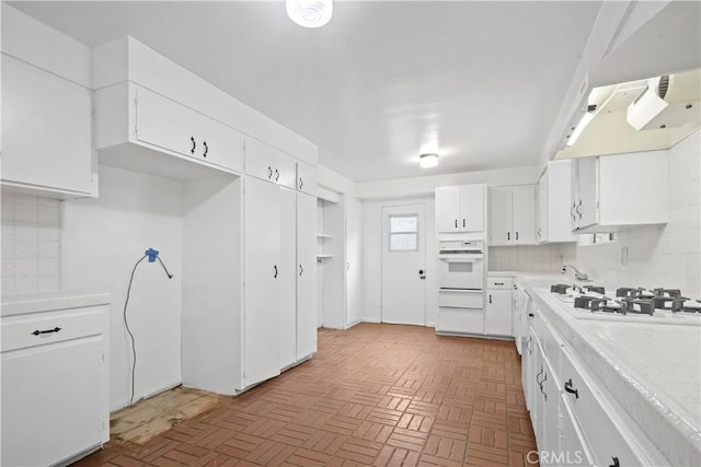 kitchen with white cabinetry, white appliances, light parquet flooring, and tasteful backsplash