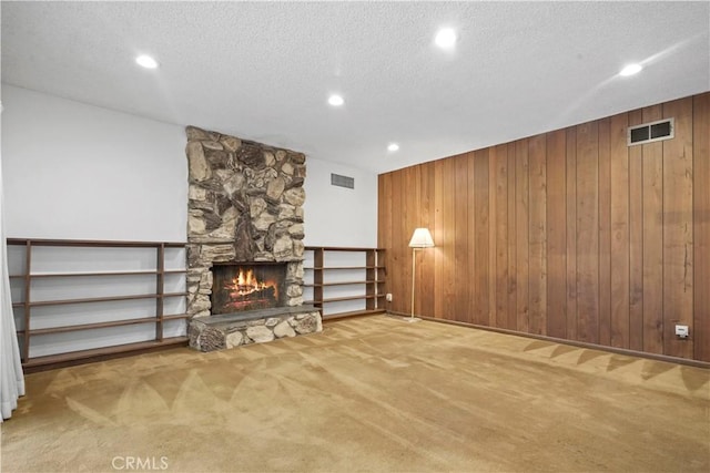 unfurnished living room with carpet flooring, a fireplace, a textured ceiling, and wood walls