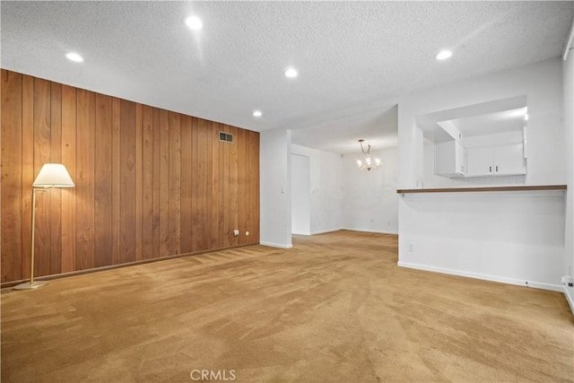 carpeted spare room with an inviting chandelier, a textured ceiling, and wood walls