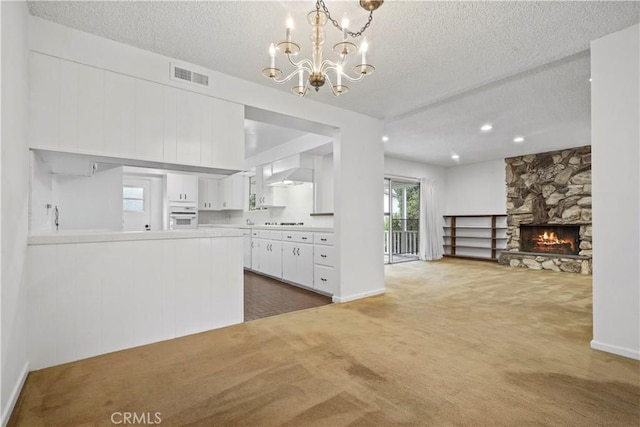 kitchen with wall chimney range hood, a stone fireplace, white cabinetry, dark carpet, and oven