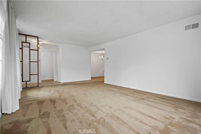 empty room with light carpet, a textured ceiling, and a chandelier