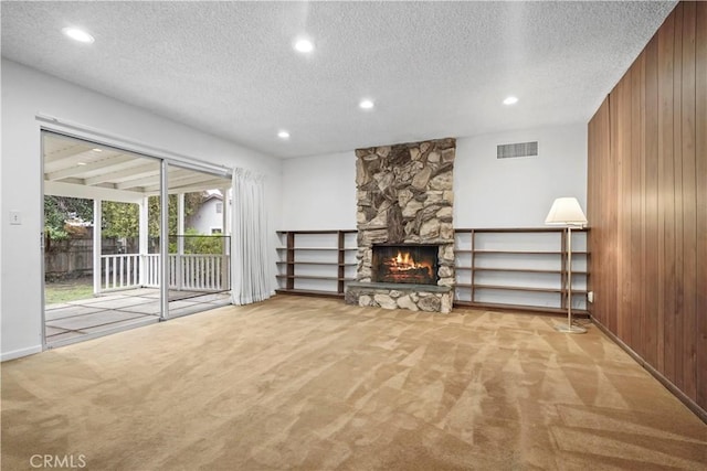 unfurnished living room with light colored carpet, a textured ceiling, a fireplace, and wood walls