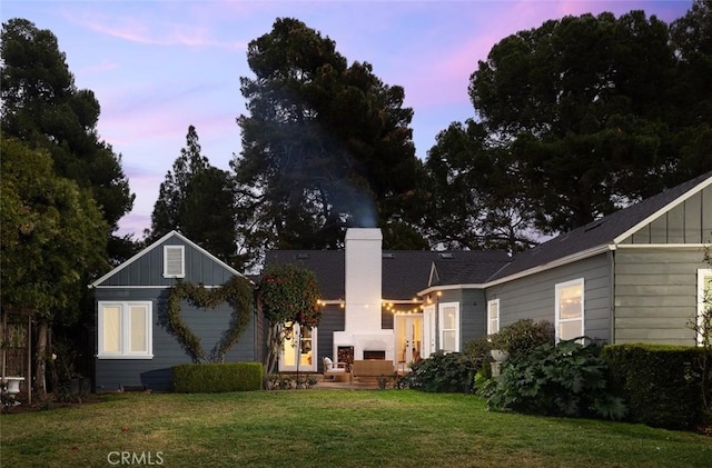 back house at dusk featuring a lawn