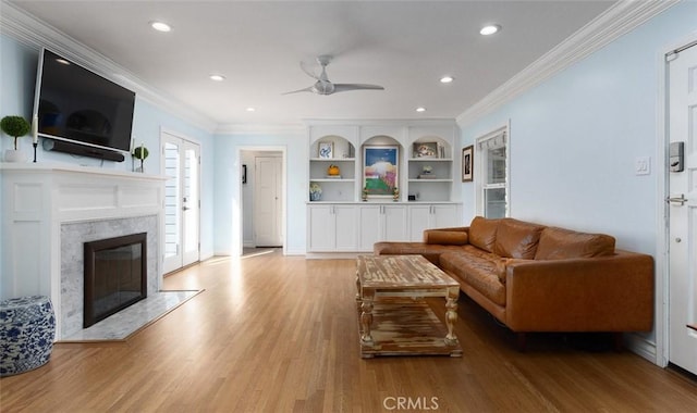 living room with built in features, ceiling fan, a high end fireplace, crown molding, and light hardwood / wood-style flooring