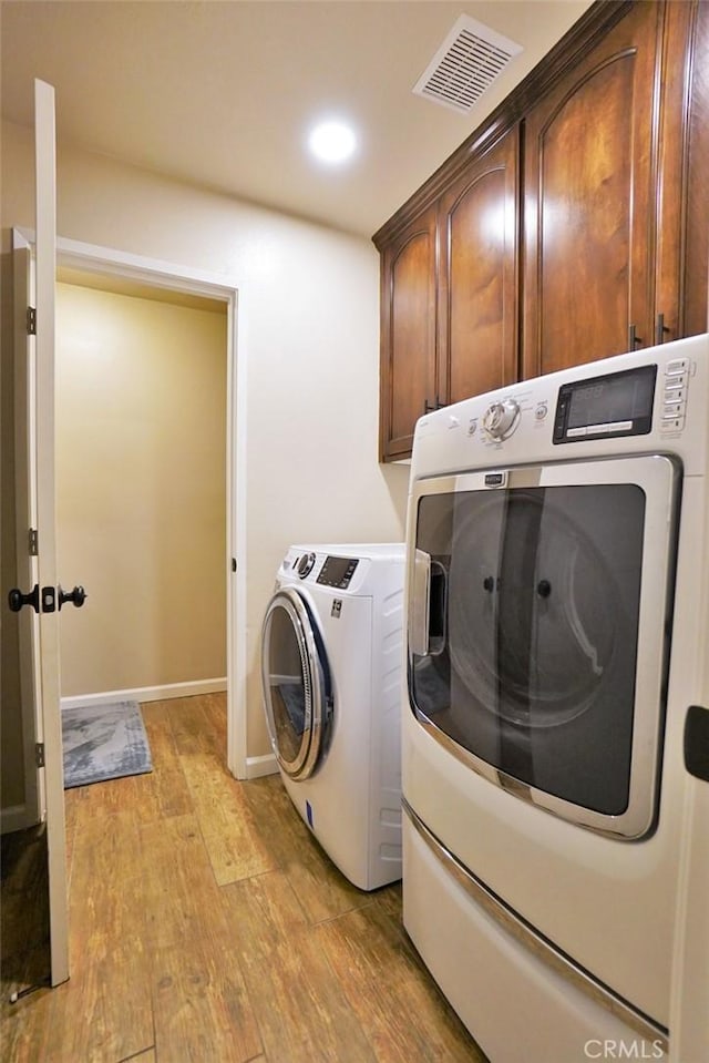 washroom featuring cabinets, washing machine and clothes dryer, and light wood-type flooring