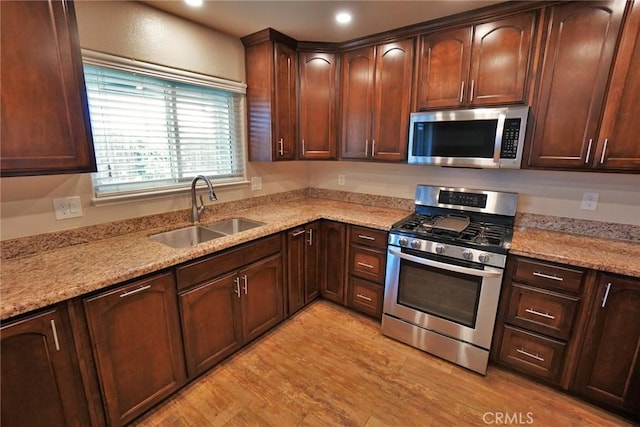 kitchen with stainless steel appliances, sink, light stone counters, and light hardwood / wood-style floors