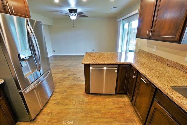 kitchen featuring appliances with stainless steel finishes, ceiling fan, kitchen peninsula, light stone countertops, and light wood-type flooring