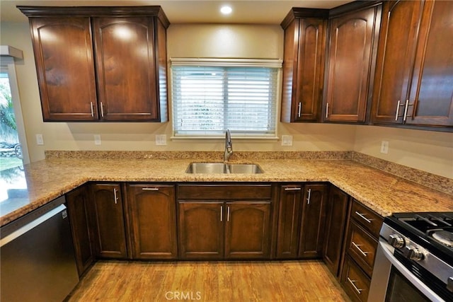 kitchen featuring stainless steel appliances, sink, light stone counters, and light hardwood / wood-style flooring