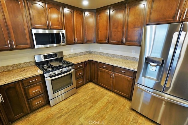 kitchen featuring stainless steel appliances, light stone countertops, and light wood-type flooring