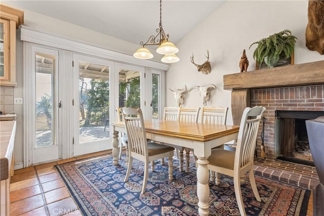 tiled dining space featuring vaulted ceiling and a brick fireplace